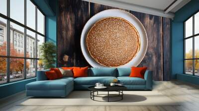 Delicious pancake sprinkled with sugar, served on a white plate on a rustic wooden table background, perfect for a sweet breakfast Wall mural