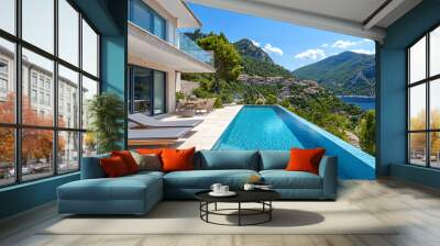 Modern infinity pool is overlooking a picturesque coastal town nestled amidst lush green mountains on a sunny day Wall mural