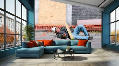 a fallen and injured construction worker in a hard hat laying on the ground at a construction work s Wall mural