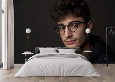 Portrait of a young adult with curly hair and eyeglasses, posing for a studio shot Wall mural