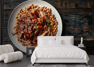 Pulled pork with bbq sauce rests on a bed of beans on a white plate against a dark wooden table Wall mural