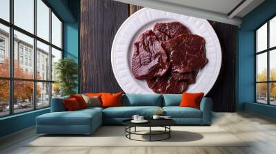 Several pieces of raw beef meat steaks lying on white plate on old wooden table, ready to be cooked Wall mural