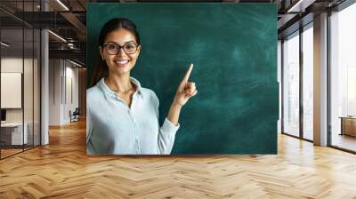 Teacher pointing and smiling at a blank chalkboard in a school classroom with space for text Wall mural