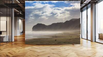 The black sand beach at Piha, New Zealand, with a strong wind blowing sand inshore. At the end of the beach is Te Waha Point Wall mural