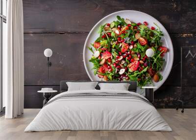 White plate with tasty salad made of arugula, tomatoes, pomegranate seeds, cucumber, herbs and spices on dark wooden table Wall mural