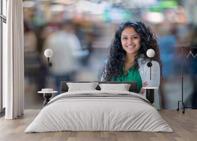 Young woman with crossed arms smiling in a busy shopping center, with a blurred background Wall mural