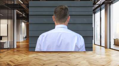 Rear view of a man standing facing a grey exterior wall Wall mural