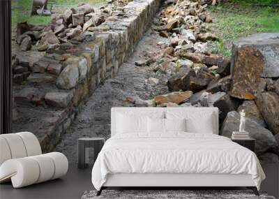 an old stone wall is being reconstructed between the two plots. the stones are dismantled and re-glued to the cement mortar. stonemason builds a wall in the park. the joints are repaired and the bush Wall mural