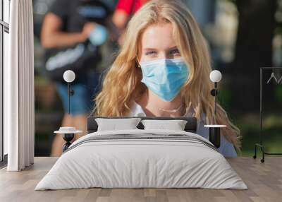 Beautiful blonde hair young girl wearing mask and promoting vaccine in the street with red cross on a white t-shirt during summer holidays Wall mural