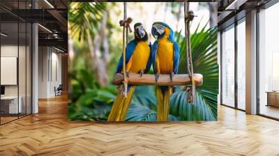 two vibrant blue and yellow parrots sit closely on a wooden swing surrounded by lush green foliage the parrots appear affectionate creating a charming and lively scene in a tropical environment Wall mural