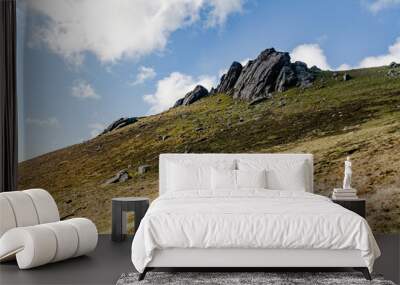 A view towards Irish hill with dark rocks sticking out of the ground and grass rocky slope with blue sky and white clouds above Wall mural