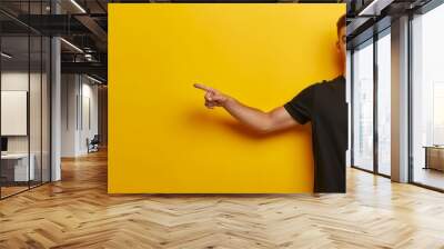 Studio photo of young man standing on left isolated on yellow background pointing at blank space for your advertisement in black t shirt seeing something unusual or unexpected. Generative ai Wall mural