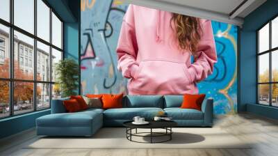 young woman with a pink hoodie and a wall with graffiti in the background. girl stays outdoor against graffiti wall, exuding urban chic.. Clothing mockup. Generative ai Wall mural