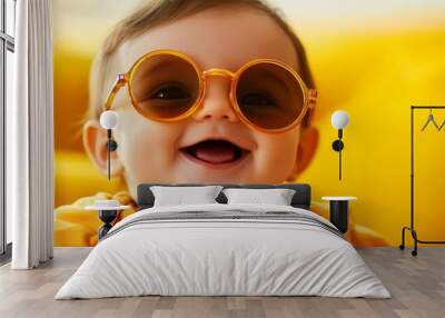 A cheerful baby wearing round sunglasses smiles broadly, radiating pure joy and innocence. The bright yellow background enhances the vibrant mood, evoking a sense of happiness and carefree fun. The ba Wall mural