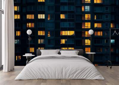 A close-up shot of a tall apartment building at night, showcasing the warm glow of the windows illuminating the dark facade. The image symbolizes urban life, community, home, and the rhythm of daily l Wall mural