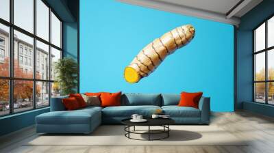 A single fresh turmeric root floats against a vibrant blue background, symbolizing health, vitality, and the power of natural ingredients. The bright yellow color represents sunshine and optimism, whi Wall mural