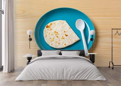 A single pita bread rests on a vibrant blue plate, accompanied by a white spoon, showcasing simplicity and freshness. The warm, golden-brown pita bread contrasts beautifully with the cool blue backgro Wall mural