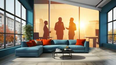 A team of three business professionals stand in silhouette against a backdrop of a city skyline, showcasing their success and ambition. The setting sun casts a warm glow, symbolizing the end of a prod Wall mural