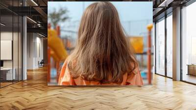 A woman with long brown hair stands looking at a colorful playground, reflecting on childhood memories, dreams, and possibilities. Wall mural