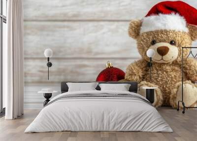 Festive Teddy Bear with Christmas Ornaments on Wooden Background - A teddy bear wearing a Santa hat sits amidst red and gold Christmas ornaments on a whitewashed wooden background, symbolizing joy, wa Wall mural