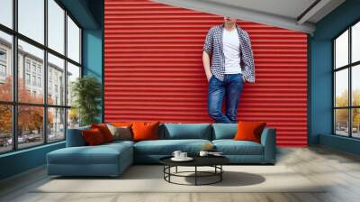 Young handsome man in a shirt and jeans near the red gate Wall mural