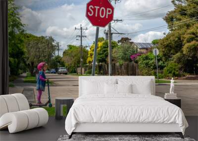 Young girl in pink outfit and pink helmet riding a kick-scooter, waiting at crossing with stop sign Wall mural