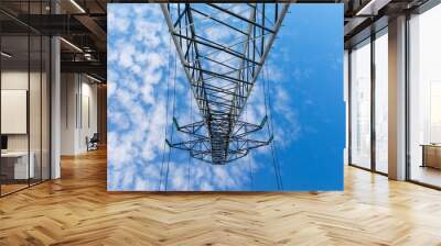 Power lines on metal pillars against a blue sky with clouds, bottom view Wall mural