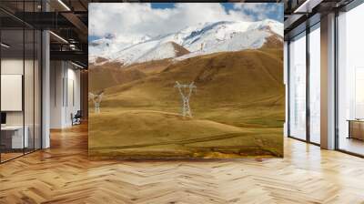 pylons of high-voltage power lines in the mountains, snowy mountain peaks and blue sky Wall mural