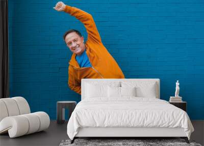 Happy elderly male stretching in front of a blue wall Wall mural