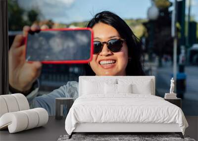 Asian woman with sunglasses taking a selfie with the phone in the city Wall mural