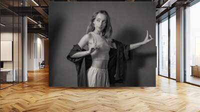 A young woman artistically poses with expressive gestures, dressed in a stylish casual outfit, standing in a studio setting with professional lighting equipment. Wall mural