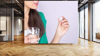 Young Caucasian woman in green sweater and white shirt holding a pill and a glass of water. Medicine and health care concept. Wall mural