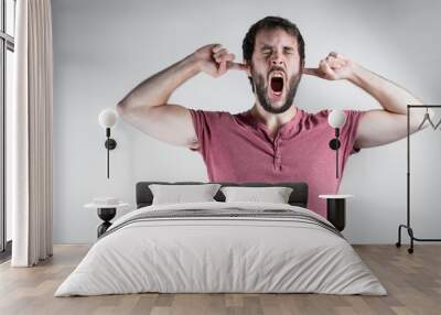 Young beard man with a grimace of suffering, screaming while covering his ears. Mental health, stress and anxiety mood. On a white background. Wall mural