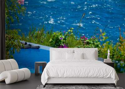 View of a swimming pool among green plants and flowers on a terrace above the sea Wall mural