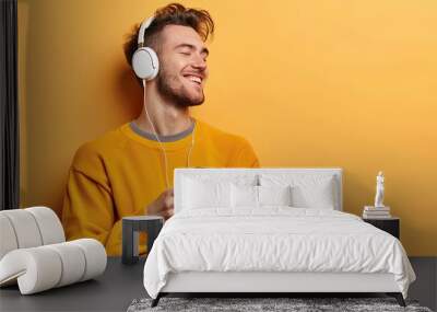 Handsome Caucasian boy, eyes closed, listening to music with headphones connected to the phone, yellow background Wall mural