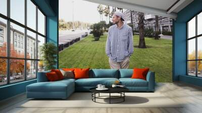 A man sits contentedly on a grassy lawn, enjoying a summer evening amidst tall palm trees and modern buildings, exuding a sense of peace and relaxation. Wall mural