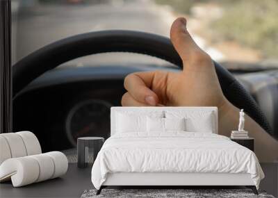 first person view of driver showing thumb up in front of steering wheel Wall mural