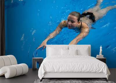 happy girl learning how to swim in the swimming pool, holding blue pool board in the water Wall mural