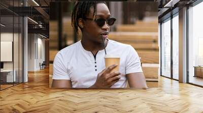 young black man sitting outdoors in cafe and drink cup of coffee, dinner time, coffee break Wall mural