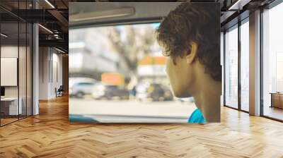 young teenager sitting on the back seat of the car and looking through the window Wall mural