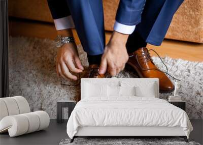 A man ties up his shoelaces on his brown shoes in the room. Wall mural