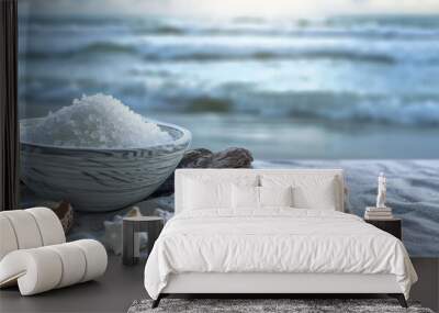 A serene coastal scene with a bowl of sea salt on weathered driftwood, surrounded by seashells and a blurred ocean in the background, capturing the pe Wall mural