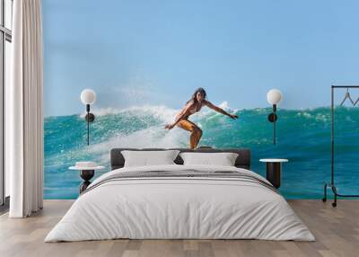 Beautiful young brunette girl in a bikini swimsuit ride wave. Sporty surfer woman surfing in Mauritius in the Indian Ocean on the background of blue sky, clouds and transparent waves. Outdoor Active. Wall mural