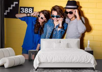 Lifestyle portrait of beautiful best friend hipsters wearing stylish bright outfits and sunglasses and having great time. In front of yellow brick wall enjoying day off and have fun. Wall mural