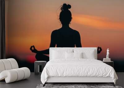 A silhouette of a woman meditating in the lotus position, capturing a serene and tranquil moment Wall mural