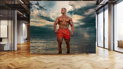 Fit athlete bodybuilder on the beach. Attractive young man lifeguard on a tropical seashore. A thunderstorm is behind the man. Wall mural