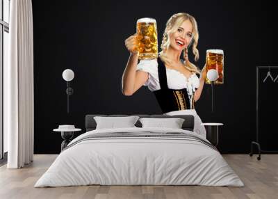 Happy sexy oktoberfest girl waitress, wearing a traditional Bavarian or german dirndl, serving two big beer mugs with drink isolated on black background. Wall mural