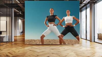 Two fit women, athletes are standing on the blue sky background before run. Healthy lifestyle and sport. Fitness concept. Wall mural