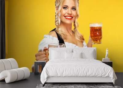 Young sexy Oktoberfest girl waitress, wearing a traditional Bavarian or german dirndl, serving two big beer mugs with drink isolated on yellow background. Wall mural