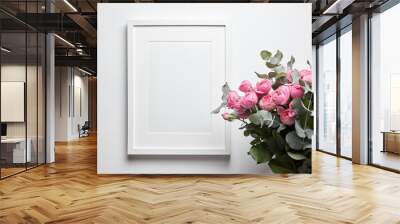 Blank frame mockup with passe-partout hanging on white wall and pink flowers in interior. White frame and floral decor Wall mural